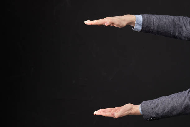 istock Man in a jacket holds an object between the palm of his hand on a black background. 1220540603