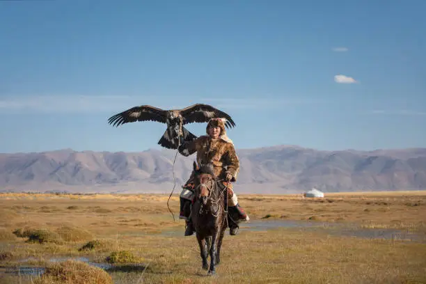 Photo of A young eagle hunter with his eagle and horse.