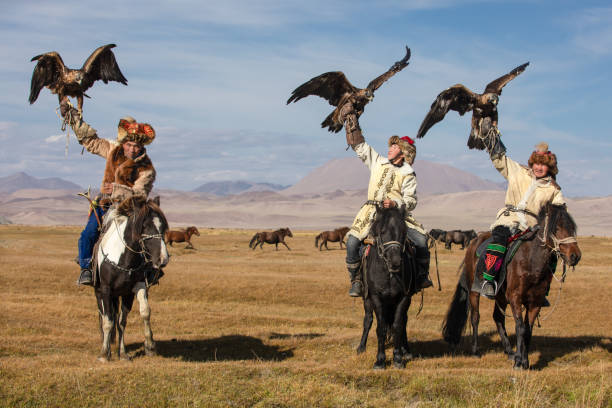 A group of eagle hunters holding their golden eagles on horseback. A group of traditional kazakh eagle hunters holding their golden eagles on horseback with a heard of horses running in the background. Ulgii, Mongolia. kazakhstan stock pictures, royalty-free photos & images