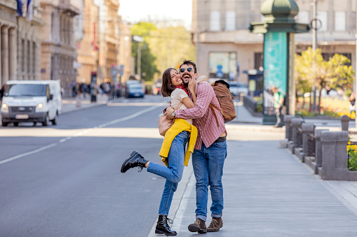 Handsome Young Man with Beard in Plaid Shirt is Feeling in Love with his Attractive Girlfriend with Long Hair while Walking in the Street. Lovely Tourist Couple is Sharing Sweetest Emotions on a Spring Day in the City.