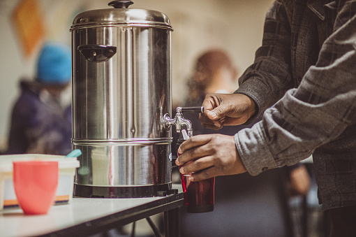 Pouring a Hot drink from a Hot water urn at a homeless shelter during lockdown
