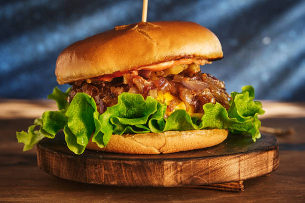 istock Burger with beef and caramelized onions on a wooden board. Cheeseburger with onion and beef. Juicy Delicious Homemade Burger. 1220545322