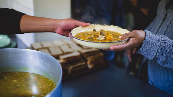 Passing of a plate with stew soup and bread kitchen food handouts to the homeless and poor during Lockdown