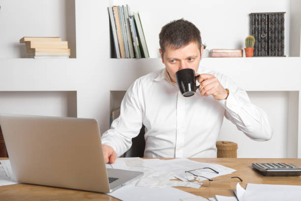 istock young businessman using laptop at home. Young man working on computer at his house.  He is drinking coffee 1220545450
