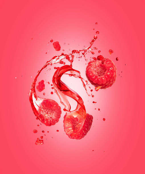 Juice splashes out from cutted raspberries on a pink background