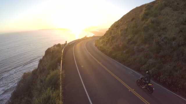 Motorbike driving on a highway by the coast during a stunning sunset in California