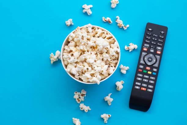 istock Popcorn and remote control viewed from above on blue background. Flat lay of pop corn bowl. Top view 1220556935