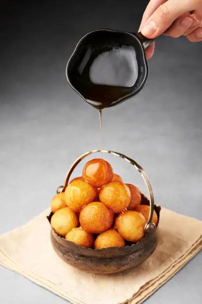 Loukoumades, luqaimat or lokma with syrup in vintage metal cup on grey concrete background. Loukoumades is eastern cuisine donunts popular during Ramazan. Popular Ramadan Food. Iftar and Suhur sweets.
