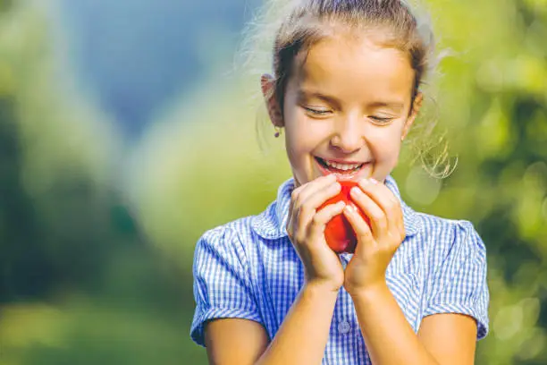 Organic food concept. Hungry female kid is ready to taste an autumnal apple, enjoying annual harvest in apple-trees garden.