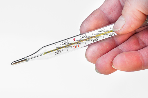 old woman holding a mercury thermometer which shows a high temperature.