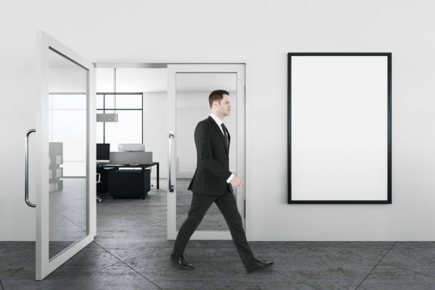 istock Businessman walking in office interior with embty banner on wall. 1220567043
