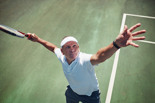 High angle shot of a handsome mature sportsman playing tennis alone on a court during the day