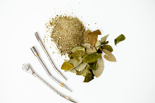Crushed Yerba Mate Tea and Coca Leaf on Display with Three Bombilla Stick Accessory for Drinking Mate Tea - Stock Photo