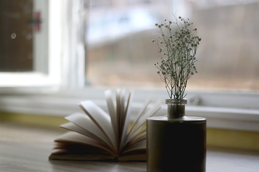 Golden vase with gypsophila flowers and an open book on a table. Selective focus.
