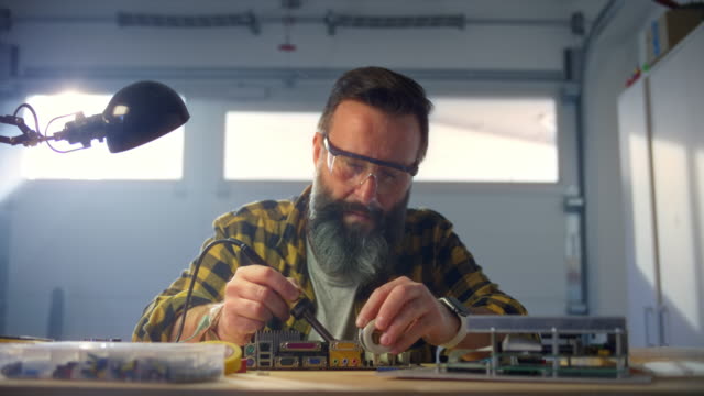 SLO MO Man repairing a circuit board by soldering it in his workshop