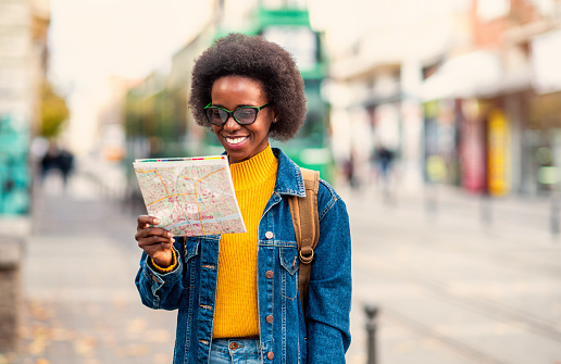 Beautiful smiling African-American woman holding a city map on the street.