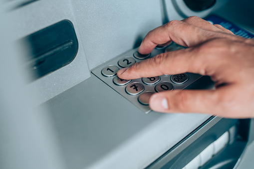 Close-up shot of man's hand withdrawing cash from ATM putting PIN entry