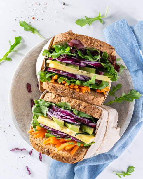 close up healthy sandwiches with arugula, carrot, cheese, red cabbage, wrapped in craft organic paper on a marbre plate and marbre white background. top view. big club sandwich concept, still life. - sandwich photos et images de collection