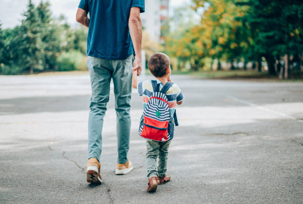 Father and son going to kindergarten. Rear view of father who leads a little boy hand in hand to kindergarten. Father and son with backpack walking in schoolyard. backpack stock pictures, royalty-free photos & images