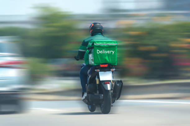 食品配達ドライバーは、オンラインで注文する顧客に製品を提供するために運転しています。流行の影響 - motorcycle biker sport city ストックフォトと画像