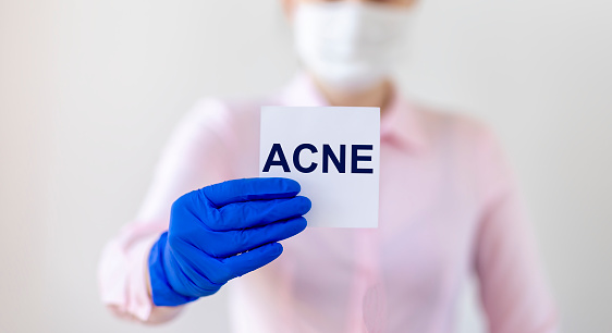 ACNE inscription on a sticker in the hand of a doctor in a blue medical glove, blurred background