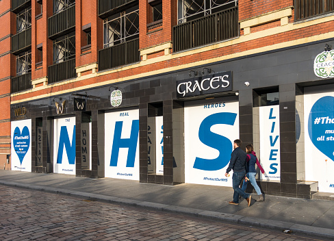 Glasgow, Scotland - A couple passing Grace's Sports Bar in Merchant City, with the pub closed and boarded up with a tribute to NHS workers.
