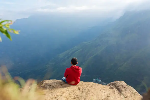 Photo of A man enjoying the mountain scenery on the edge of a cliff.