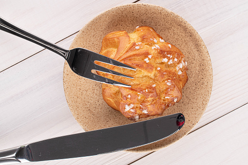 One whole fresh baked profiterole with fork and knife on white wood