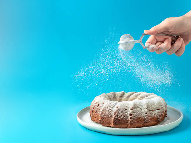istock Female hand sprinkling icing sugar on bundt cake 1220605852