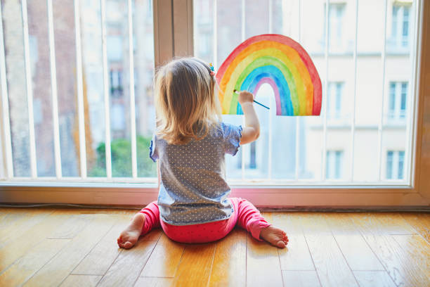 窓ガラスに虹を描く愛らしい幼児の女の子 ストックフォト
