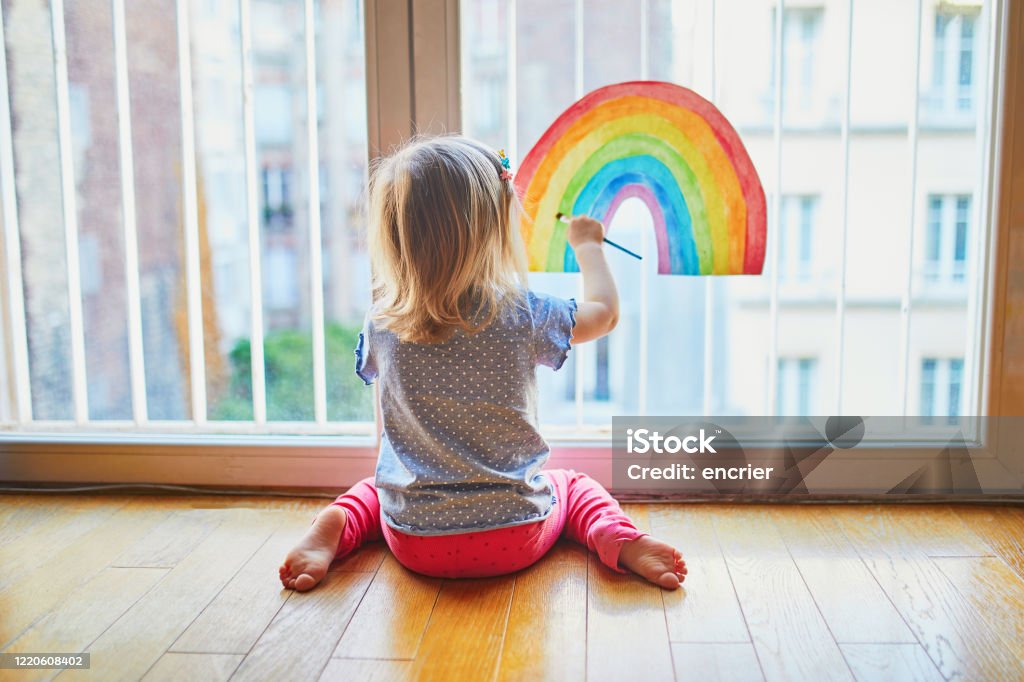 Adorable toddler girl painting rainbow on the window glass Adorable toddler girl painting rainbow on the window glass as sign of hope. Creative games for kids staying at home during lockdown. Self isolation and coronavirus quarantine concept Child Stock Photo