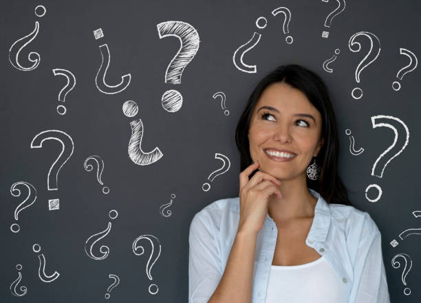 Portrait of a thoughtful woman looking at question marks on a blackboard