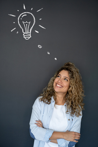 Thoughtful woman having a bright idea and looking at a light bulb on a blackboard