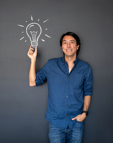 Portrait of a creative man having a bright idea and pointing at a light bulb on a blackboard