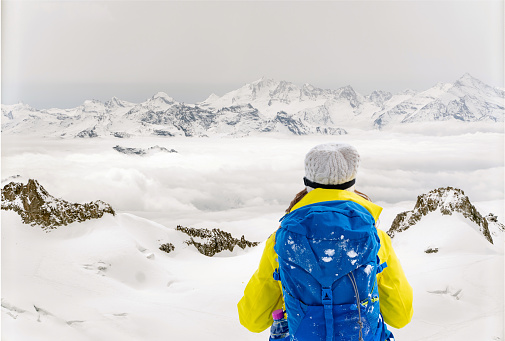 Hiker reaching the top of the mountain and looking at the snow while carrying her backpack