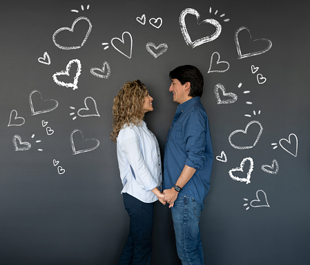 Loving couple looking very happy holding hands with hearts drawn on a blackboard around them