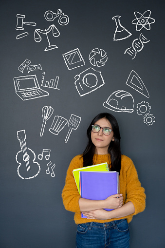 Happy student thinking about what to study as her major and looking at the options on a blackboard â education concepts