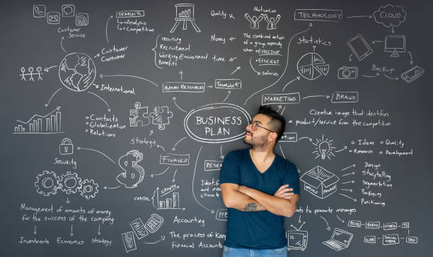 Thoughtful entrepreneur looking at the business plan behind him Happy Latin American thoughtful entrepreneur looking at the business plan behind him on a blackboard business plan stock pictures, royalty-free photos & images