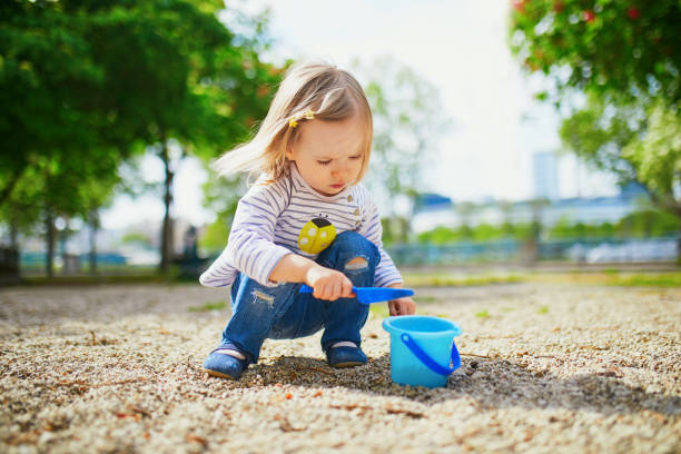Adorable toddler girl playing with bucket and shovel Adorable toddler girl playing with bucket and shovel, making mudpies and gathering small stones. Outdoor creative activities for kids sandbox photos stock pictures, royalty-free photos & images