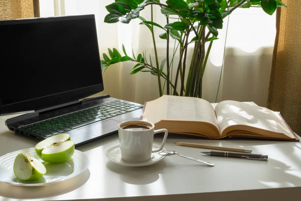 A workplace with a computer, an open book, an apple and a cup of coffee.