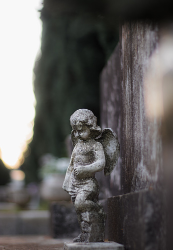 Small sculpture of a baby angel with wings on a stone grave tombstone. Old dirty worn over time