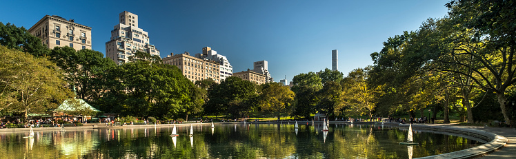 Luxury high end apartment and condominium panoramic residences rise up over the Conservatory Water and the Manhattan skyline in Central Park in New York City USA