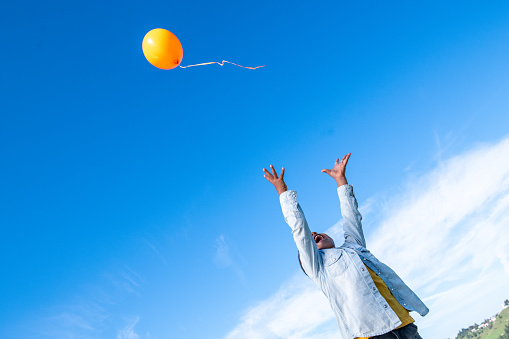 Smiling boy releasing orange balloon in blue sky.