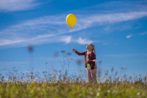 istock Girl holding balloon against blue sky 1220625256