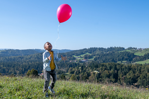 Smiling boy releasing pink balloon in blue sky while standing in field.