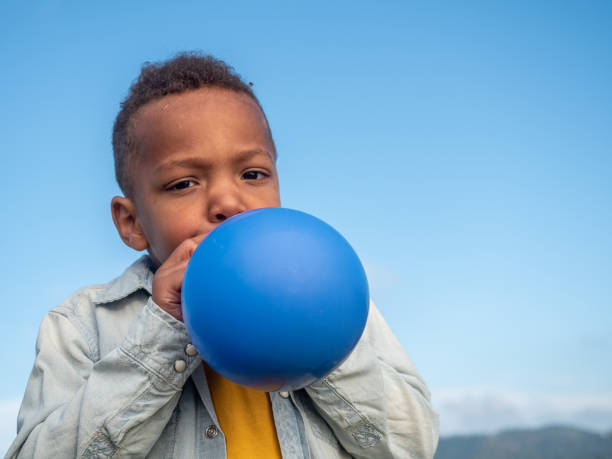 маленький мальчик взрывает воздушный шар - child balloon outdoors little boys стоковые фото и изображения