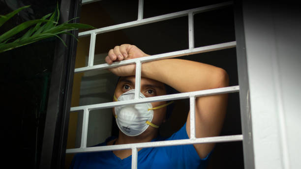 istock Latin man with white face mask inside his house looking out through the window, leaning against security bars 1220626335