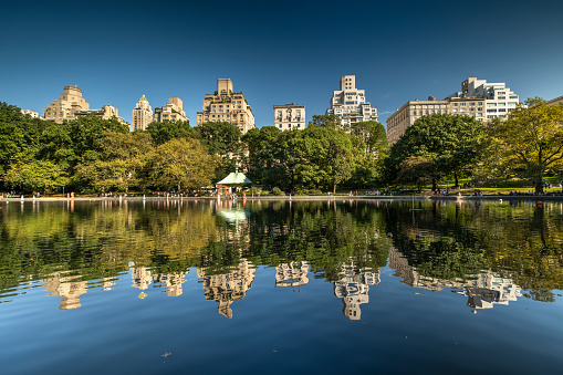 Luxury high end apartment and condominium residences rise up over the Conservatory Water and the Manhattan skyline in Central Park in New York City USA