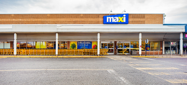 Maxi Supermarket facade panoramic view on a cloudy day with a long line of empty carts. Photographed in Montreal on Easter day during Covid lockdown. Maxi is the discount brand of Loblaw's grocery stores.