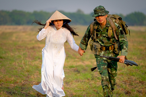 Soldier man holds hand of Vietnamese girl and run in the field with action of escape from war with love story.
